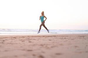 actif sportif femme courir le long de océan le surf par l'eau bassin à garder en forme et santé. le coucher du soleil le sable plage Contexte avec Soleil. femme aptitude, le jogging faire des exercices et sport activité photo