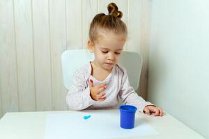 magnifique peu fille dessine avec doigt des peintures sur une blanc feuille de papier. Créatif enfant développement dans Jardin d'enfants ou gratuit temps à Accueil photo