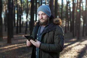 proche en haut portrait de adulte Masculin promeneur en utilisant numérique languette et à la recherche pour emplacement pendant une randonnée dans la nature. homme sur une randonnée en utilisant numérique tablette pour la navigation. photo