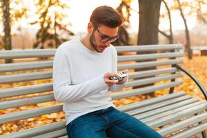 Jeune Beau branché gars des promenades dans une magnifique l'automne parc sur le Contexte de Jaune feuilles dans chaud ensoleillé temps et prend des photos sur une porc film caméra. l'automne loisir temps. Créatif jeunesse