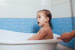 amusement de bonne humeur content bambin bébé prise une une baignoire en jouant avec mousse bulles. peu enfant dans une baignoire. souriant enfant dans salle de bains sur bleu Contexte. hygiène et santé se soucier. photo