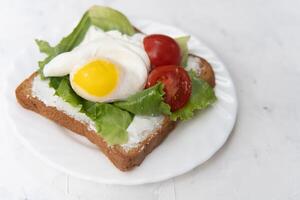 sandwich avec frit des œufs salade et tomate sur une blanc assiette sur une blanc Contexte. photo