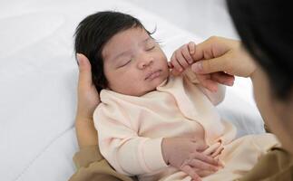 mère émouvant joue de nouveau née bébé fille sur lit à maison. bébé fille ou garçon en train de dormir sur maman bras. l'amour et Nouveau la vie concept photo