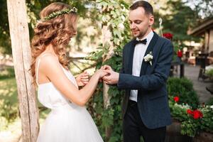 beauté la mariée et Beau jeune marié sont portant anneaux chaque autre. mariage couple sur le mariage cérémonie. magnifique modèle fille dans blanc robe. homme dans costume. femelle et Masculin portrait. mignonne Dame et gars photo