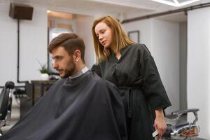 Beau bleu regardé homme séance dans coiffeur magasin. coiffeur coiffeur femme Coupe le sien cheveux. femelle coiffeur. photo