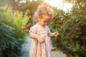 une peu fille habillé dans une à la mode robe balades dans le arrière-cour ou dans le parc sur une chaud été ensoleillé après-midi, été vacances concept photo