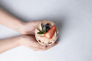 Haut vue de enfant mains en portant Chocolat petit gâteau avec crème fromage Glaçage, fruit sur béton Contexte photo