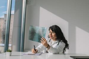 Jeune Indien médical étudiant à le clinique dans entraine toi. femelle médecin dans blanc manteau avec stéthoscope examine radiographie photo