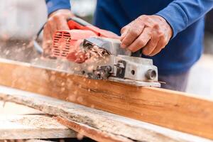 Charpentier en utilisant électrique raboteuse à lisse en dehors le bois, travail du bois machine, homme rabotage planches avec électrique outils photo