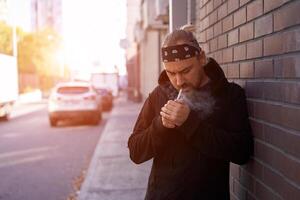 Beau Jeune non rasé homme noir sweat à capuche et bandana des stands arrière-cour près brique des murs été journée. photo