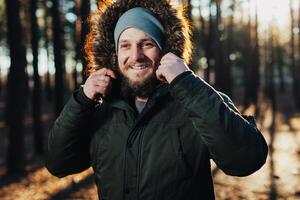 proche en haut portrait de une barbu branché touristique dans gris capuche homme dans le lumière du soleil photo