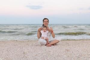 content famille mère et enfant fille Faire yoga, méditer dans lotus position sur plage à le coucher du soleil photo