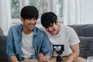 jeune couple gay asiatique couple d'influenceurs vlog à la maison. les adolescents coréens lgbtq heureux se détendent en s'amusant à l'aide de l'enregistrement de la caméra vlog vidéo upload dans les médias sociaux tout en étant allongé sur le canapé dans le salon au concept de maison. photo