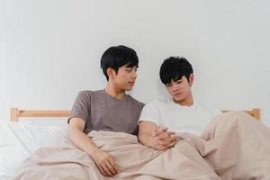 beau couple gay asiatique parlant sur le lit à la maison. jeune mec lgbtq asiatique heureux de se détendre se reposer ensemble passer du temps romantique après s'être réveillé dans la chambre à coucher à la maison moderne le matin concept. photo