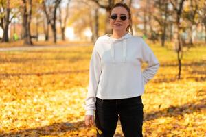 portrait de magnifique Jeune femme dans une blanc chandail et des lunettes de soleil en marchant en plein air dans l'automne photo