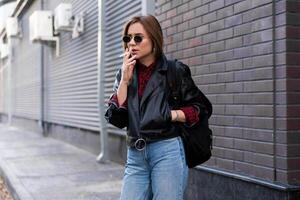 magnifique Jeune avec style habillé caucasien fille fume cigarette sur le rue. photo