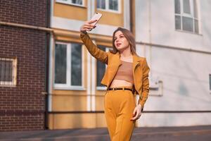 magnifique Jeune caucasien fille 20 ans vieux avec blanc cheveux habillé élégant Orange affaires costume fait du selfie sur le téléphone tandis que permanent sur le rue. photo