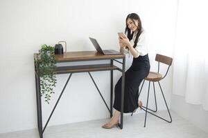 une Japonais femme vérification téléphone intelligent par éloigné travail dans le Accueil Bureau photo