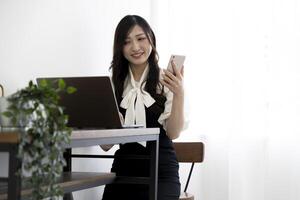 une Japonais femme vérification téléphone intelligent par éloigné travail dans le Accueil Bureau photo