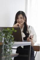 une Japonais femme vérification téléphone intelligent par éloigné travail dans le petit Bureau photo