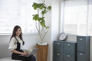 une Japonais femme vérification téléphone intelligent par éloigné travail dans le Accueil Bureau photo