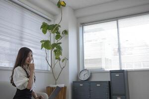 une Japonais femme vérification téléphone intelligent par éloigné travail dans le Accueil Bureau photo