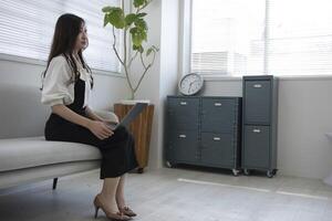 une Japonais femme vérification téléphone intelligent par éloigné travail dans le Accueil Bureau photo