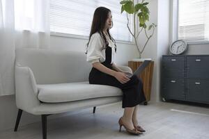 une Japonais femme vérification téléphone intelligent par éloigné travail dans le Accueil Bureau photo