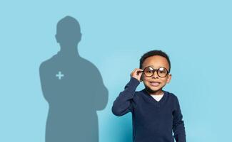 une sur de soi Jeune garçon avec des lunettes ajuste le sien cadres, souriant contre une bleu Contexte photo