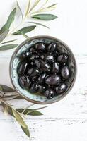 ai généré bol de brillant noir Olives sur une rustique blanc en bois surface suivant à olive branches photo