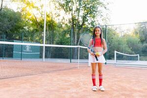 portrait de une peu fille sur le tennis tribunal photo