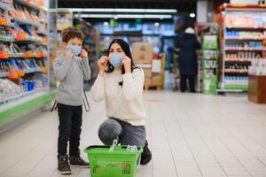 Jeune femme et sa enfant portant protecteur visage masques magasin une nourriture à une supermarché pendant le coronavirus épidémie ou grippe épidémie. photo