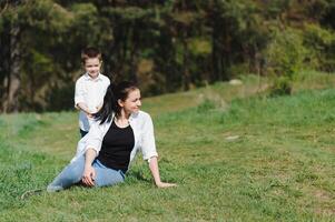 content famille mère avec fils enfant en jouant ayant amusement ensemble sur le herbe dans ensoleillé été jour, la vie moment photo