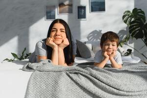 portrait de une content mère et sa les enfants fils mensonge sur une lit photo