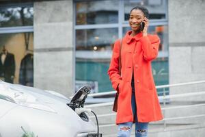 africain américain fille mise en charge électro voiture à le électrique gaz gare. photo