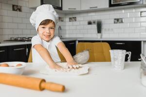 garçon dans cuisinier chapeau séance à une cuisine comptoir. peu garçon dans cuisine photo