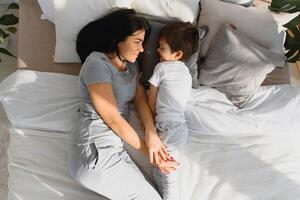 portrait de une content famille, maman et bébé dans le chambre à coucher, mère et fils sont étreindre photo