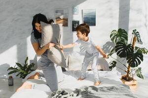 content mère et fils combat avec oreillers dans lit sur fin de semaine Matin photo