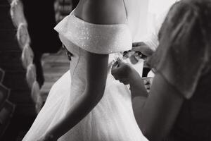 demoiselle d'honneur portion mince la mariée laçage sa mariage blanc robe, boutonnage sur délicat dentelle modèle avec duveteux jupe sur taille. Matin de mariée préparation détails jeunes mariés. mariage journée des moments, porter. photo