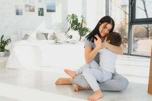 de bonne humeur mère séance sur canapé dans confortable lumière vivant pièce détient sur tour chatouille de peu fils prendre plaisir marrant Activités sur fin de semaine à maison, avoir amusement ensemble, inestimable temps avec préscolaire enfant concept photo