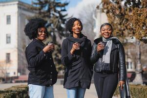 Trois élégant africain américain les filles en buvant café sur le rue et ayant amusement photo