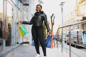 magnifique frisé aux cheveux afro américain femme permanent dans une achats centre commercial avec coloré achats Sacs dans mains. photo