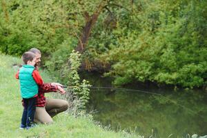 une père enseignement le sien fils Comment à poisson sur une rivière à l'extérieur dans été ensoleillement photo