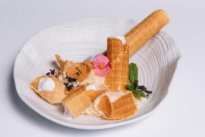 sucré dessert. tranche tubules avec une délicat protéine crème et une petit tamis avec en poudre sucre sur une blanc rond plateau sur une blanc Contexte. photo