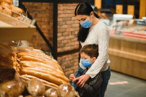 Jeune femme et sa peu fils portant protecteur visage masque magasin une nourriture à une supermarché pendant le coronavirus épidémie ou grippe épidémie. photo