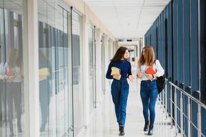 deux Jeune femmes avec livre bavardage tandis que permanent dans Université couloir. Université élèves dans couloir après le conférence. photo