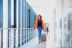 plein longueur côté portrait de Jeune noir femme en marchant avec valise dans aéroport photo