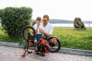 content père et le sien fils ayant amusement ensemble à le vert parc, fixation vélo ensemble. du père journée. photo