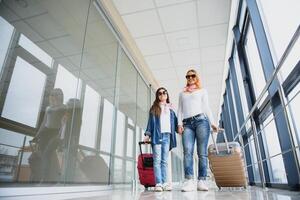 content Jeune mère et sa fille en marchant dans le aéroport Terminal tandis que porter une valise. haute saison et vacances concept. se détendre et modes de vie photo