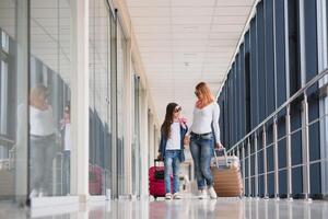 content Jeune mère et sa fille en marchant dans le aéroport Terminal tandis que porter une valise. haute saison et vacances concept. se détendre et modes de vie photo